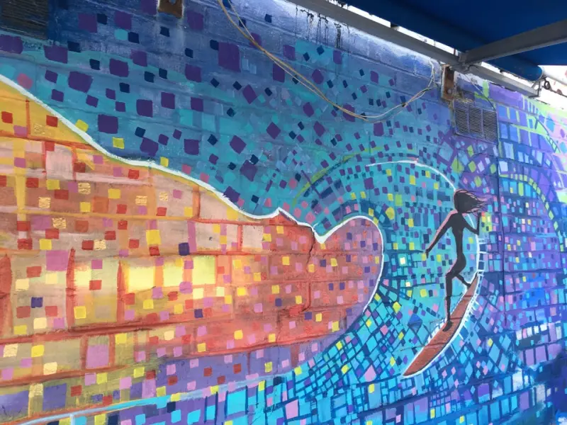 Colorful mosaic mural of a surfer riding a wave on the cafe's exterior wall