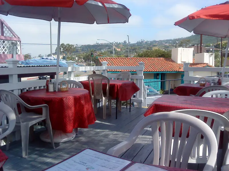 Rooftop patio dining area with red umbrellas and tablecloths overlooking the San Clemente hills