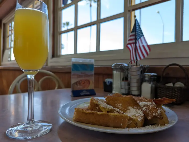 A mimosa in a champagne flute next to a plate of french toast at a sunny window table