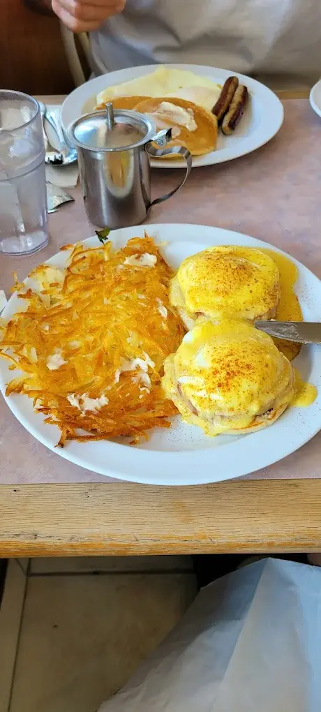 Eggs Benedict topped with hollandaise and paprika next to crispy hash browns