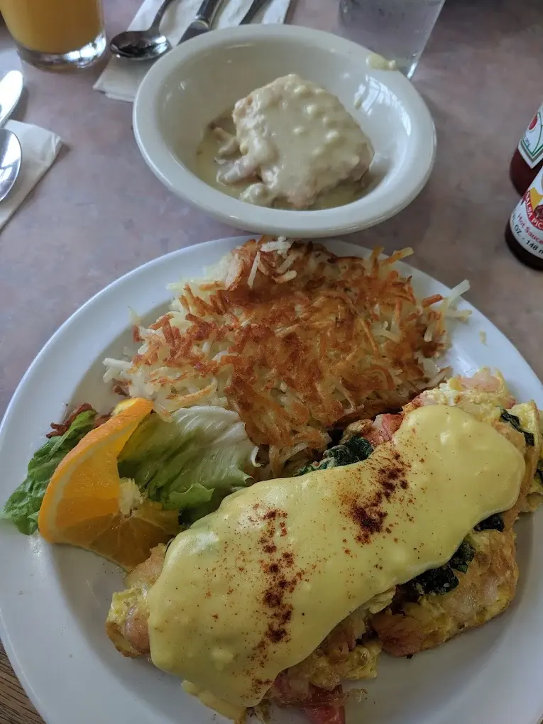 A specialty omelette topped with hollandaise next to hash browns, with a side of biscuits and gravy
