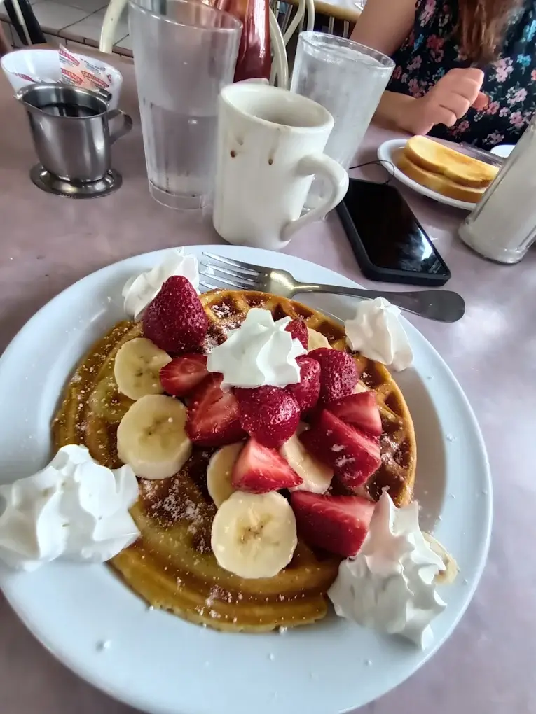 A Belgian waffle topped with strawberries, banana slices and whipped cream