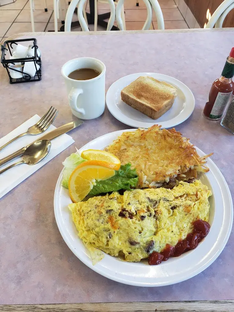 A fluffy omelette with a side of ketchup, hash browns, toast and a cup of coffee