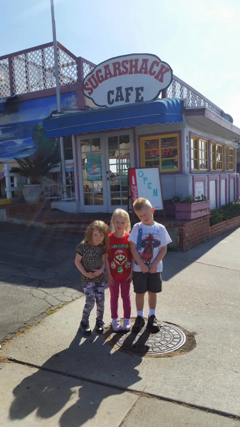 Three young kids standing in front of the Sugar Shack Cafe storefront
