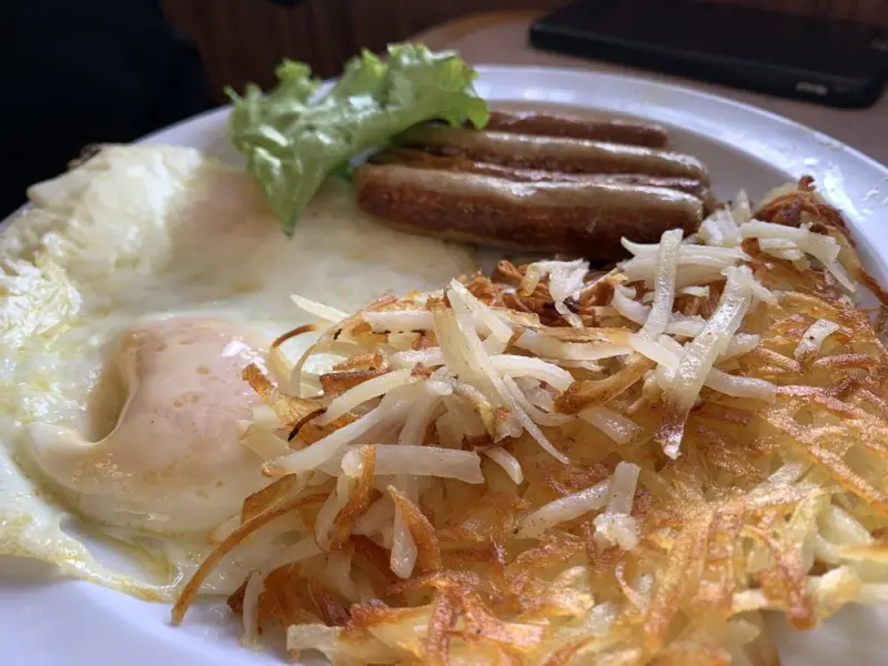 Two fried eggs with breakfast sausage links and crispy hash browns on a white plate