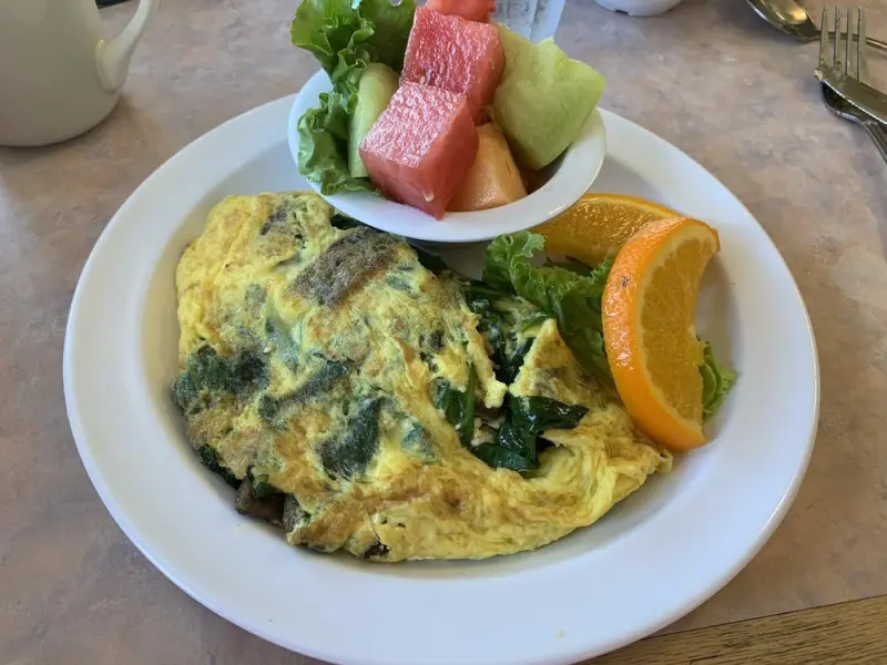 Spinach omelet served with a fresh fruit cup of watermelon and melon and an orange slice