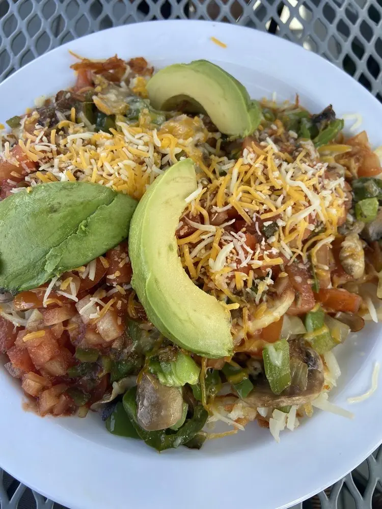 Loaded veggie breakfast hash topped with sliced avocado, shredded cheese, tomatoes and salsa