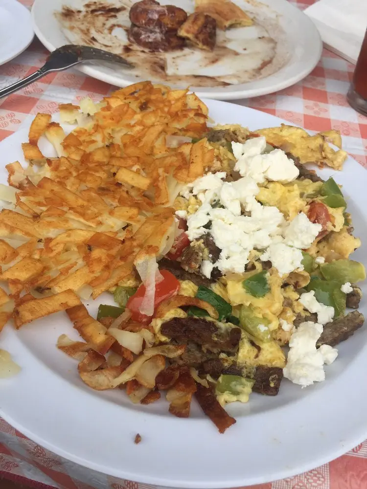 Gyro-style scramble with feta, green peppers and beef beside hash browns on a red gingham tablecloth