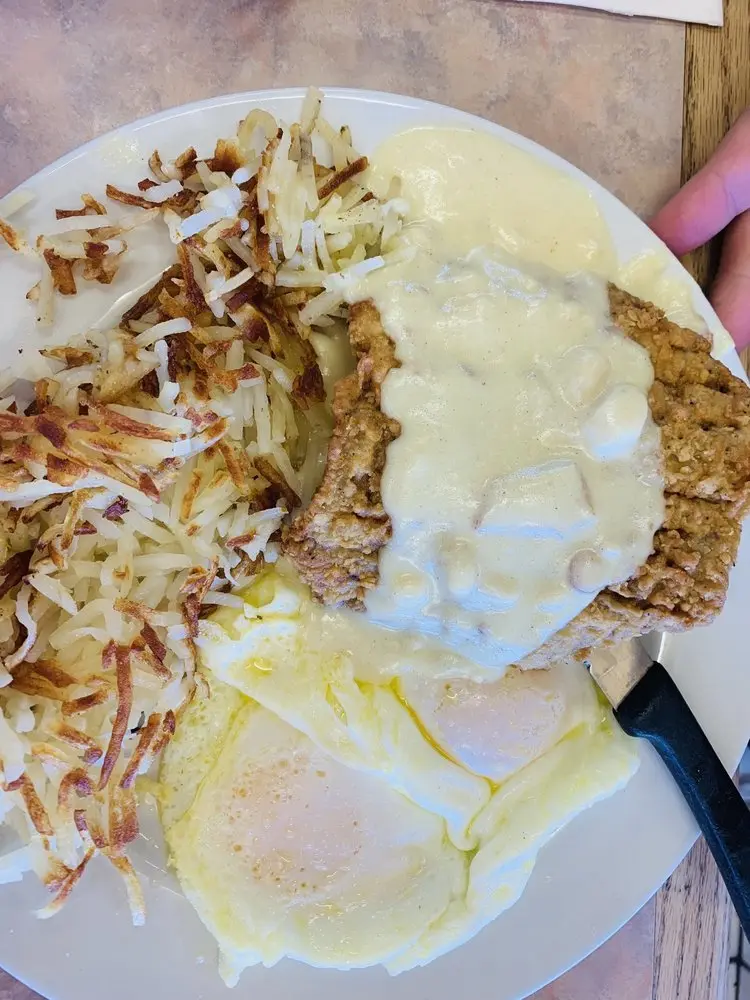 Chicken fried steak covered in country gravy with over-easy eggs and hash browns
