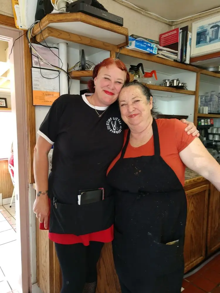 Two smiling Sugarshack Cafe staff members posing together arm in arm behind the counter
