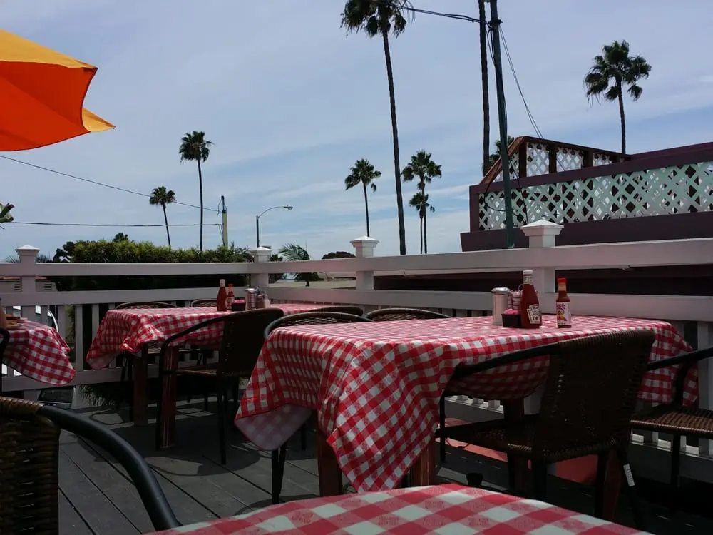 Rooftop patio with red gingham tables, colorful umbrellas and palm trees under a bright blue sky