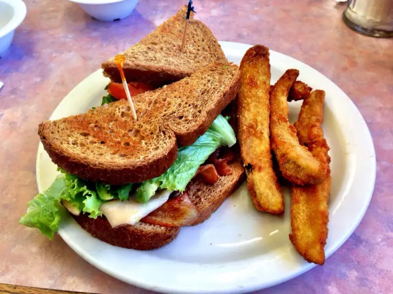 Turkey club sandwich on toasted wheat bread with lettuce, tomato and bacon, plated with crispy fried zucchini sticks