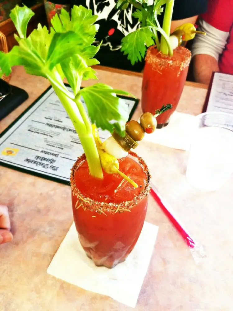 Two garnished Bloody Mary cocktails with salted rims, celery stalks, olives and pickles on a cafe table