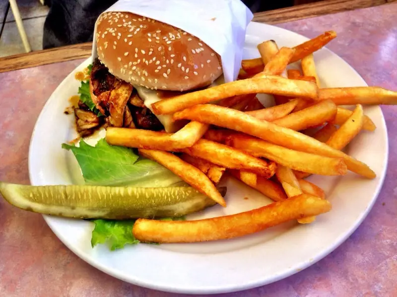 Grilled chicken sandwich with melted cheese on a sesame bun, served with golden French fries and a pickle spear