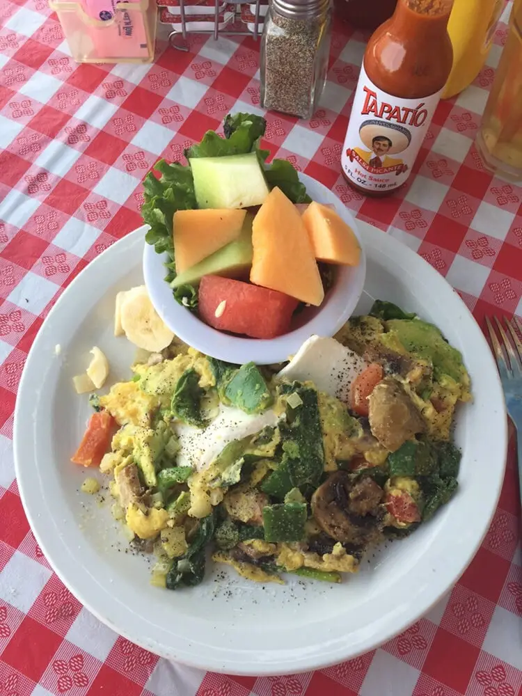 Veggie scramble with mushrooms, spinach and avocado served with a bowl of fresh melon and banana