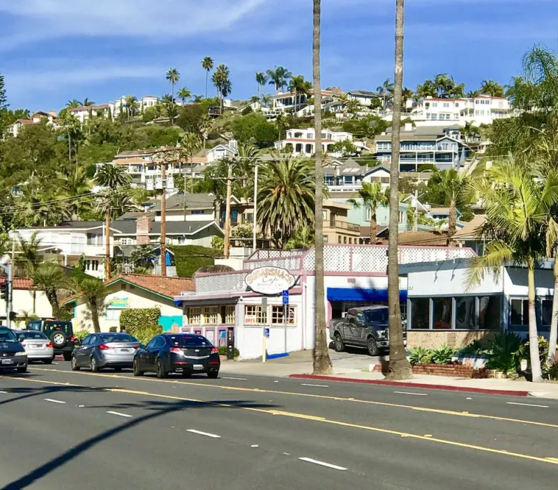 Wide street view of the Sugar Shack Cafe on El Camino Real backed by palm trees and the San Clemente hillside