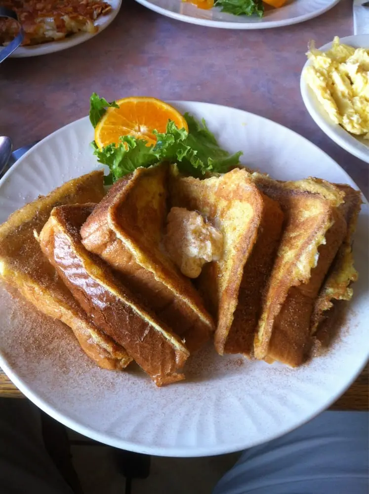 Thick golden slices of cinnamon French toast topped with butter and served with an orange slice