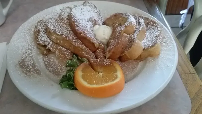Slices of French toast fanned across a plate, dusted with powdered sugar and garnished with an orange