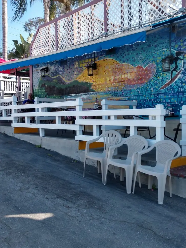 Cafe patio beside a vibrant surfer mosaic mural under palm trees