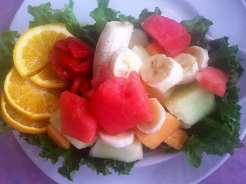 Vibrant fresh fruit plate of orange, strawberry, banana, watermelon and melon on leafy greens