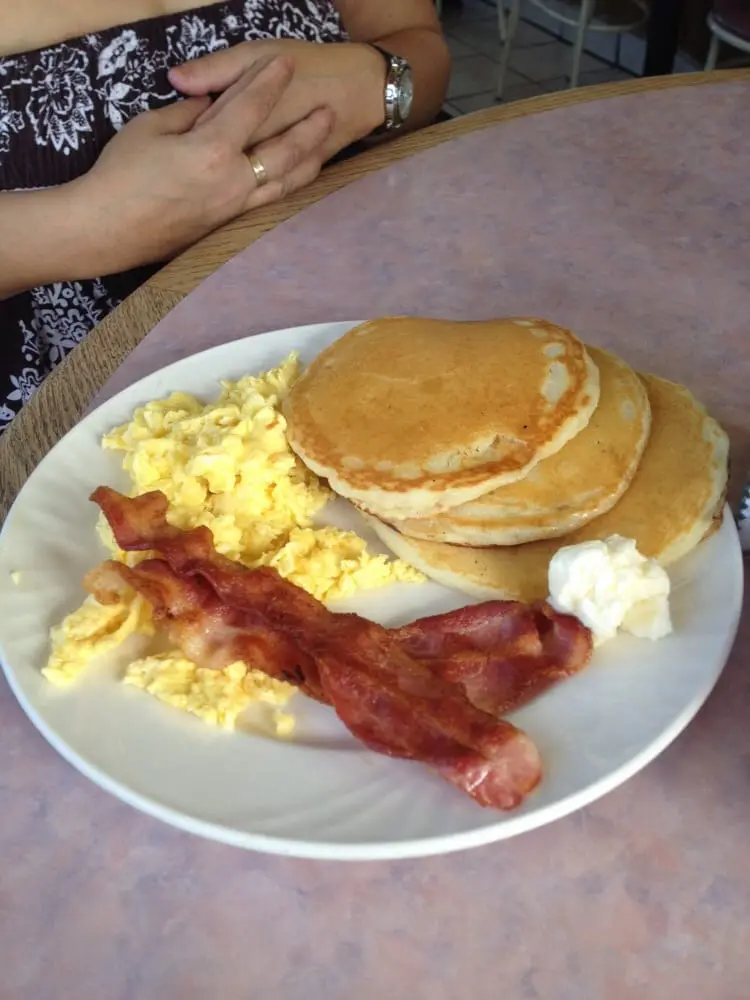 Stack of golden pancakes with scrambled eggs and crispy bacon