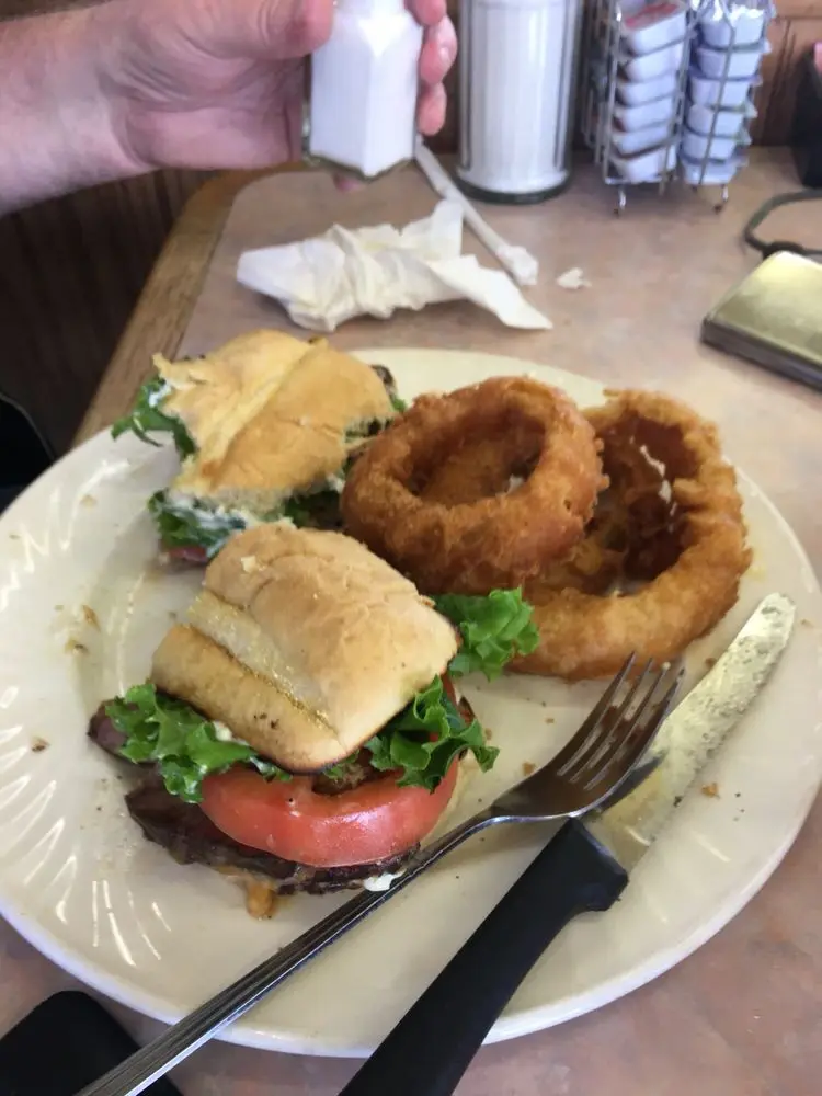 Burger cut in half with lettuce and tomato served alongside golden onion rings
