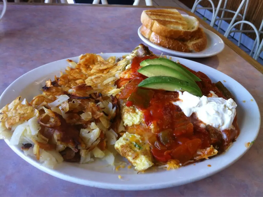 Ranchero omelette topped with salsa, sour cream and avocado beside crispy hash browns