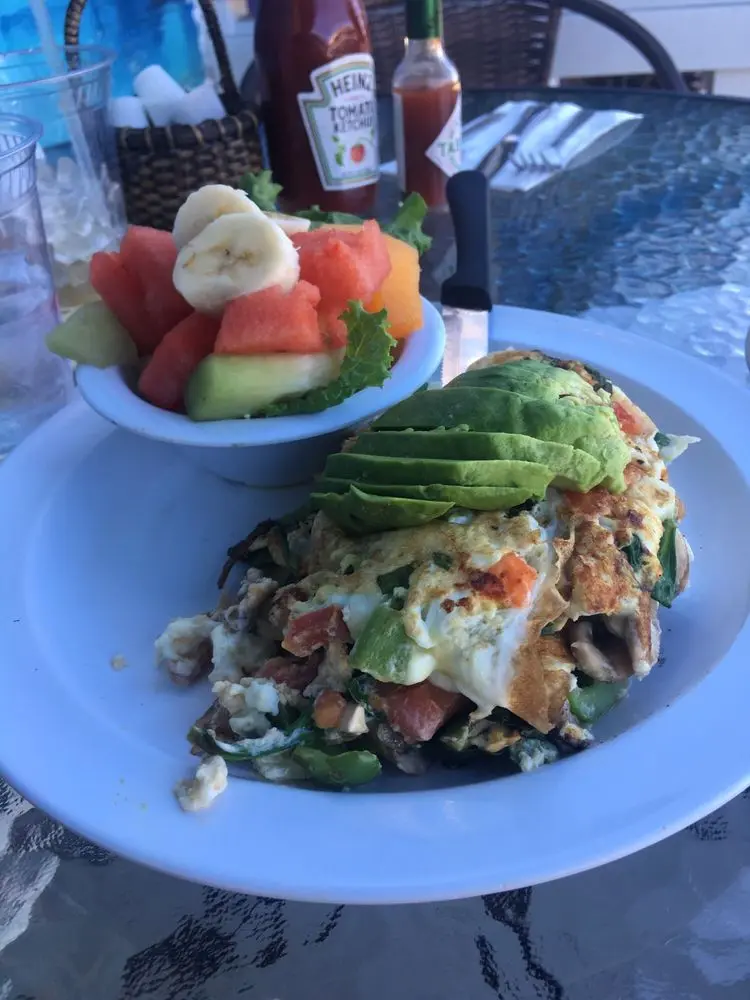 Veggie omelette crowned with avocado slices next to a bowl of fresh cut fruit