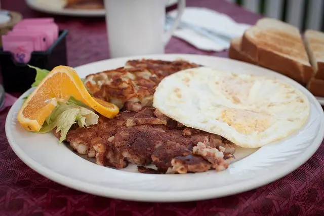 Corned beef hash with a fried egg, hash browns, toast and an orange garnish