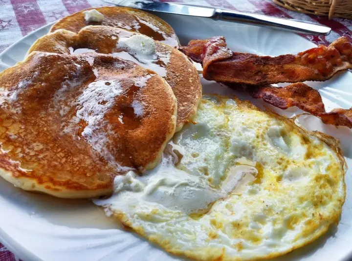 Golden pancakes with over-easy eggs and crispy bacon on a white plate